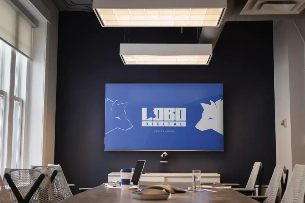 Photo-Mockup_-123-scaled-1webp | Lobo Digital | Lobo Digital Conference room with a dark wall and a large blue LOBO DIGITAL banner on the wall behind the table